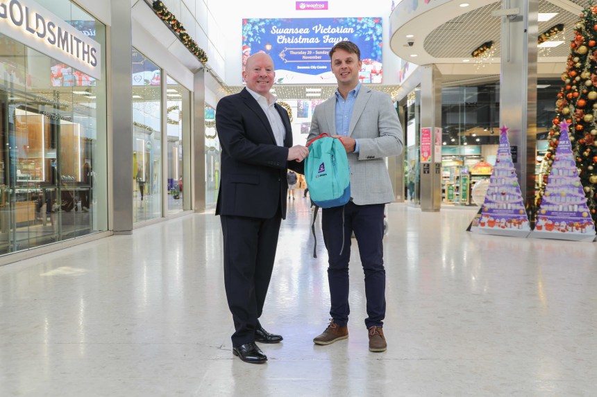 Julian John and Adam Gibbons shake hands inside Swansea’s Quadrant Shopping Centre, holding a sensory pack.