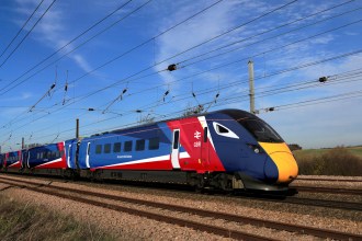 Electric GBR train with Union Flag colours travelling through rural UK landscape