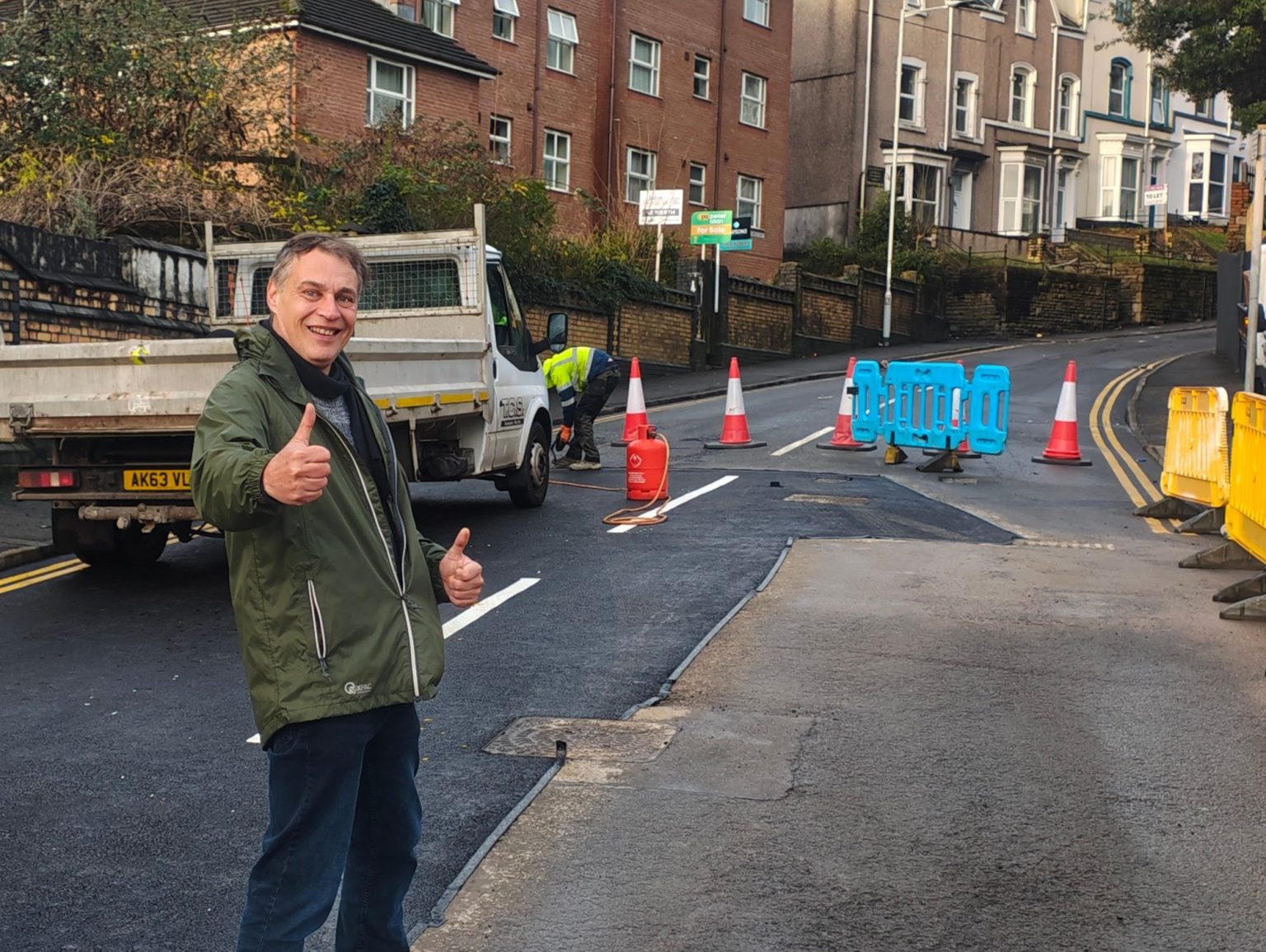 Cllr Peter May standing with thumbs up in front of repaired Brynymor Road in Swansea.