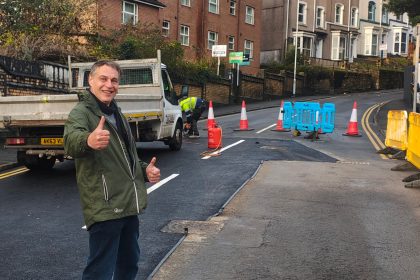 Cllr Peter May standing with thumbs up in front of repaired Brynymor Road in Swansea.