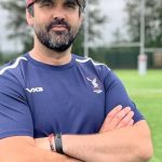 Jonathan Thomas wearing Swansea RFC kit and red cap, standing on the training field with arms crossed.