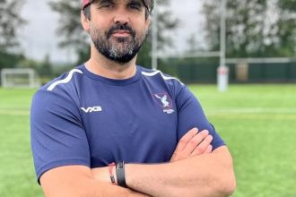 Jonathan Thomas wearing Swansea RFC kit and red cap, standing on the training field with arms crossed.
