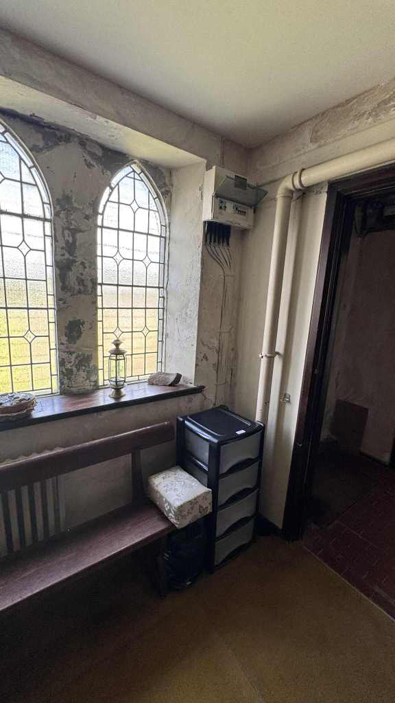 Corner of St David’s Church with arched leaded glass windows, peeling plaster, exposed pipes, and modern storage units.