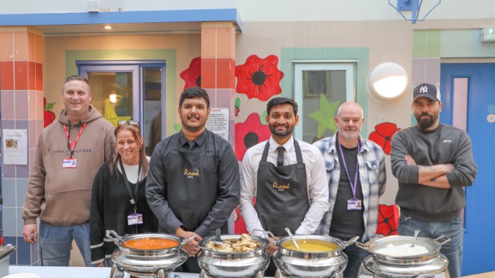 Group of Rasoi staff and volunteers behind buffet table serving Indian food at community event in Swansea.
