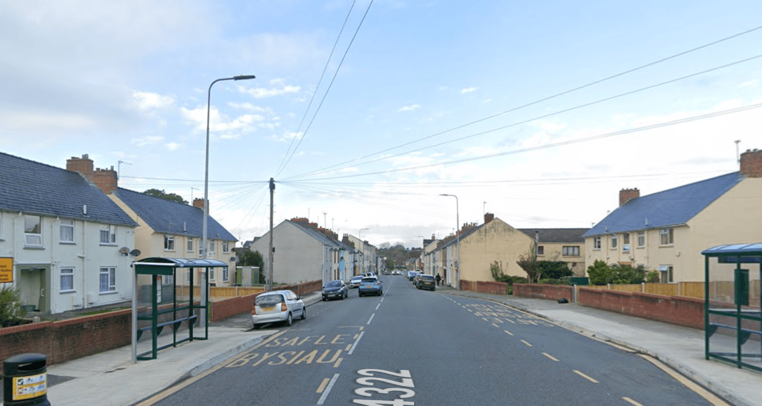 Residential street in Pembroke Dock with bus stops, parked cars, and semi-detached houses on Laws Street.