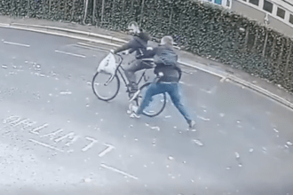 Surveillance still showing a plain‑clothes officer intercepting a cyclist during a shoplifting arrest in Swansea.