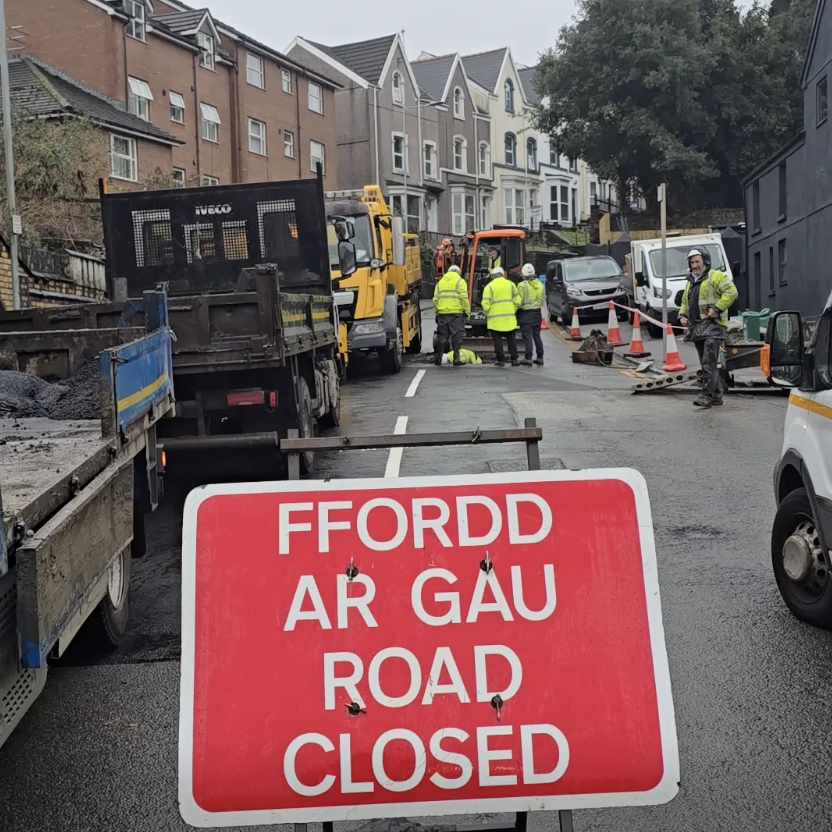 Road closed sign with highways crews at Brynymor Road sinkhole site.