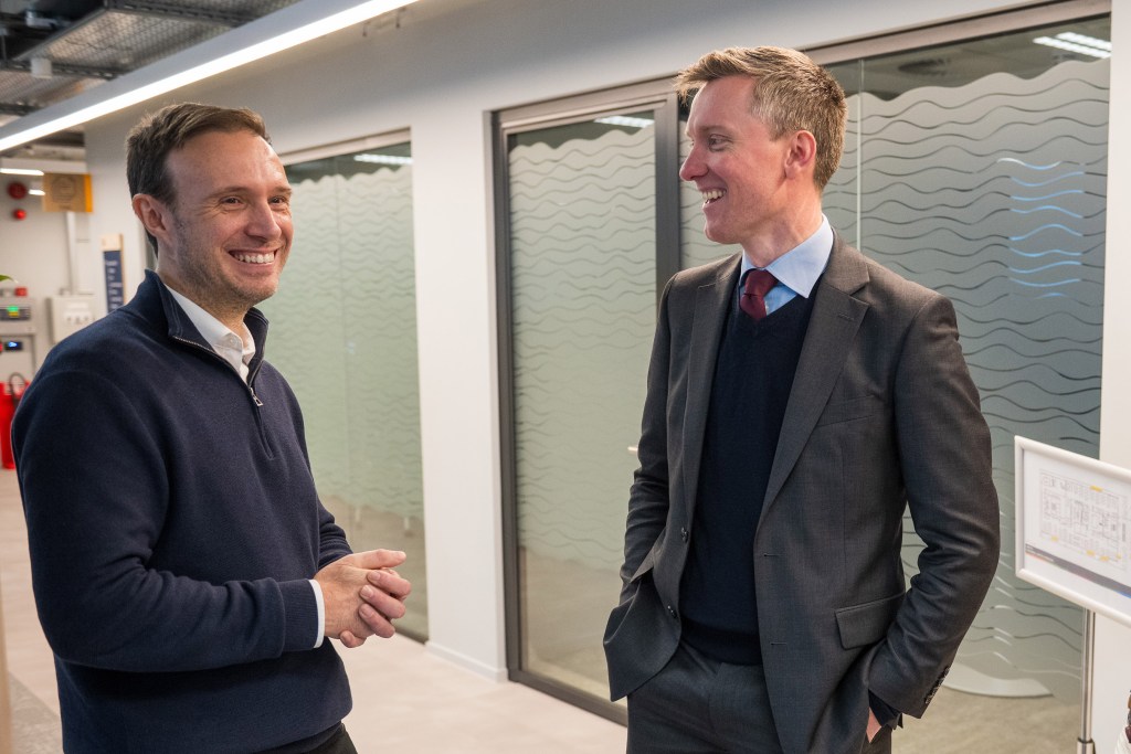 Matt Warren and Torsten Bell talking inside Veeqo’s Swansea HQ near glass doors.