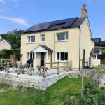 Cream-coloured detached house with solar panels and raised patio seating area in rural Carmarthenshire.