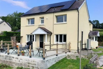 Cream-coloured detached house with solar panels and raised patio seating area in rural Carmarthenshire.