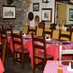 Interior of a rustic pub dining room with red tablecloths, wooden furniture, wine bottles on display, and traditional decor.