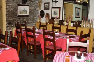 Interior of a rustic pub dining room with red tablecloths, wooden furniture, wine bottles on display, and traditional decor.
