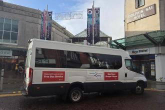 Shopper Hopper minibus outside Quadrant Shopping Centre in Swansea, with bilingual signage and nearby shops.