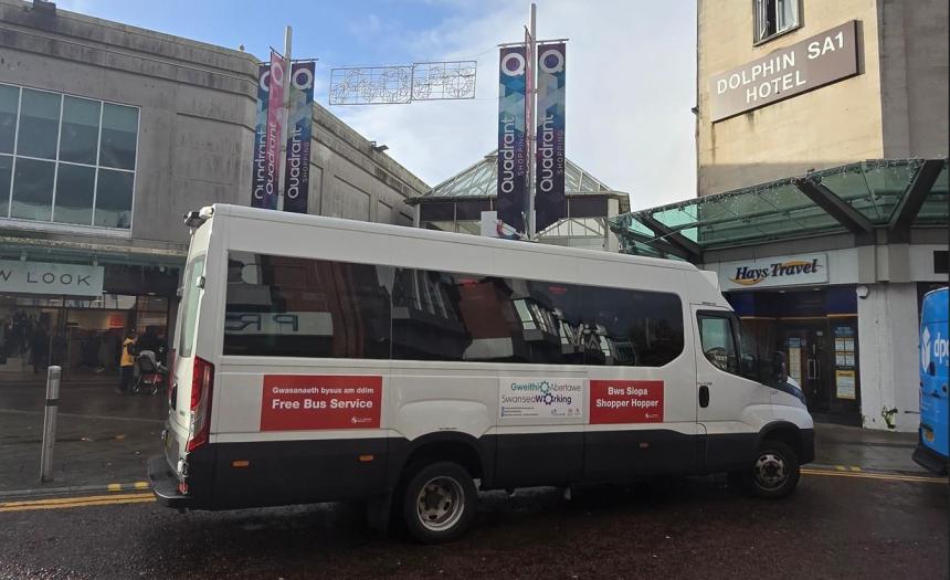 Shopper Hopper minibus outside Quadrant Shopping Centre in Swansea, with bilingual signage and nearby shops.
