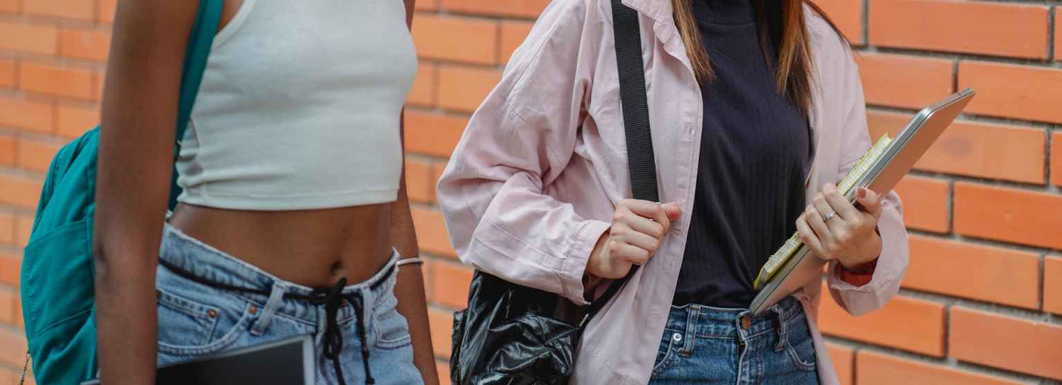 crop black student walking with female friend near brick wall