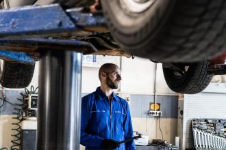 man in blue coverall standing under a vehicle with a tool