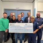 Group of Kenfig Hill firefighters and Morriston Hospital cardiac staff holding a large fundraising cheque after a sponsored walk.