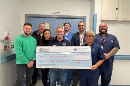 Group of Kenfig Hill firefighters and Morriston Hospital cardiac staff holding a large fundraising cheque after a sponsored walk.
