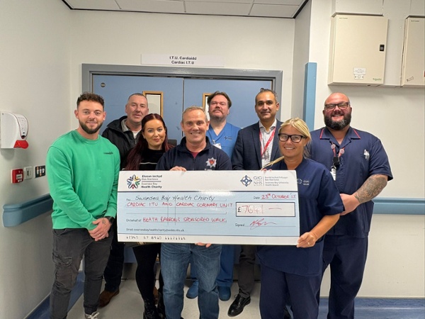 Group of Kenfig Hill firefighters and Morriston Hospital cardiac staff holding a large fundraising cheque after a sponsored walk.