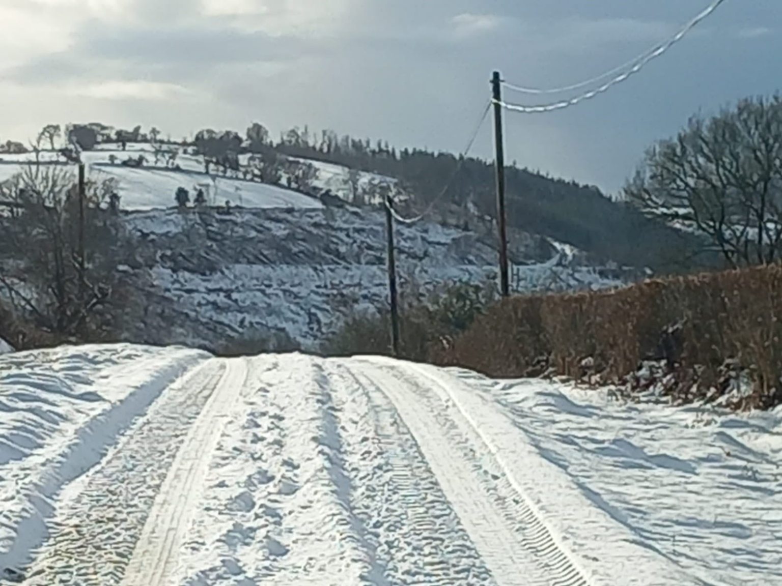 Snow-covered country road with tire tracks and hedgerows, photographed during winter conditions in Carmarthenshire.