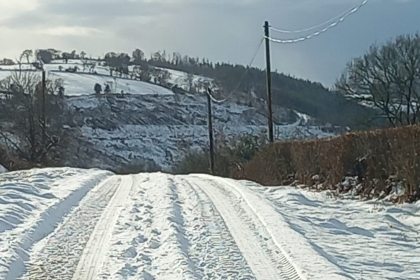 Snow-covered country road with tire tracks and hedgerows, photographed during winter conditions in Carmarthenshire.