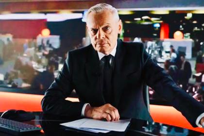 Martin Clunes in character as Huw Edwards, sitting at a BBC‑style newsreading desk in a promotional image for the Channel 5 drama.
