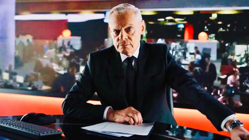 Martin Clunes in character as Huw Edwards, sitting at a BBC‑style newsreading desk in a promotional image for the Channel 5 drama.