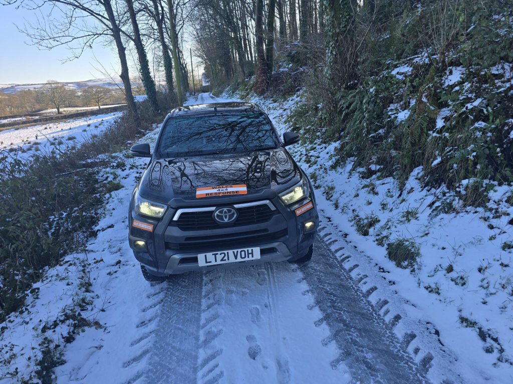 Snow-covered country road with tire tracks and hedgerows, photographed during winter conditions in Carmarthenshire.