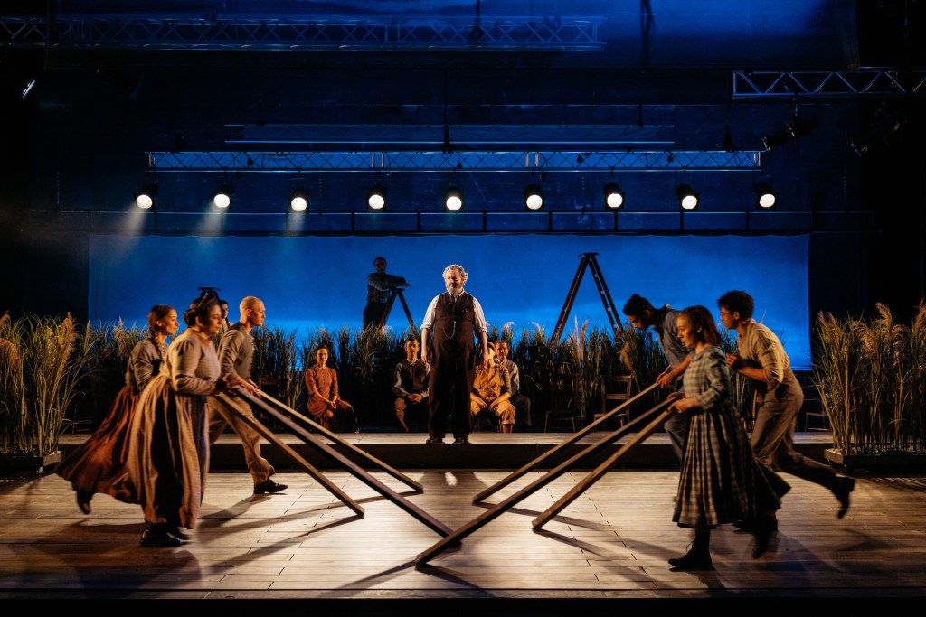 Ensemble cast in Our Town performing with wooden frames on stage. Image: Welsh National Theatre.