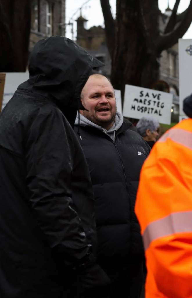Dean Ronan at a Maesteg Hospital protest, standing among demonstrators holding placards opposing closure plans.