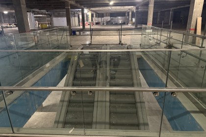 View down escalators inside empty Debenhams with exposed ceiling and construction fencing.