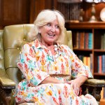 Fiona Hughes sitting in an armchair with a bookcase and dark wood panelling in the background during her time on The Traitors.