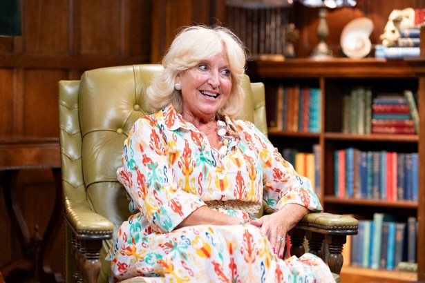 Fiona Hughes sitting in an armchair with a bookcase and dark wood panelling in the background during her time on The Traitors.