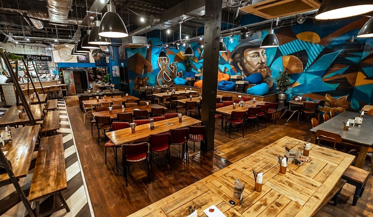 Founders & Co Swansea communal dining area with mural, long tables and relaxed seating.