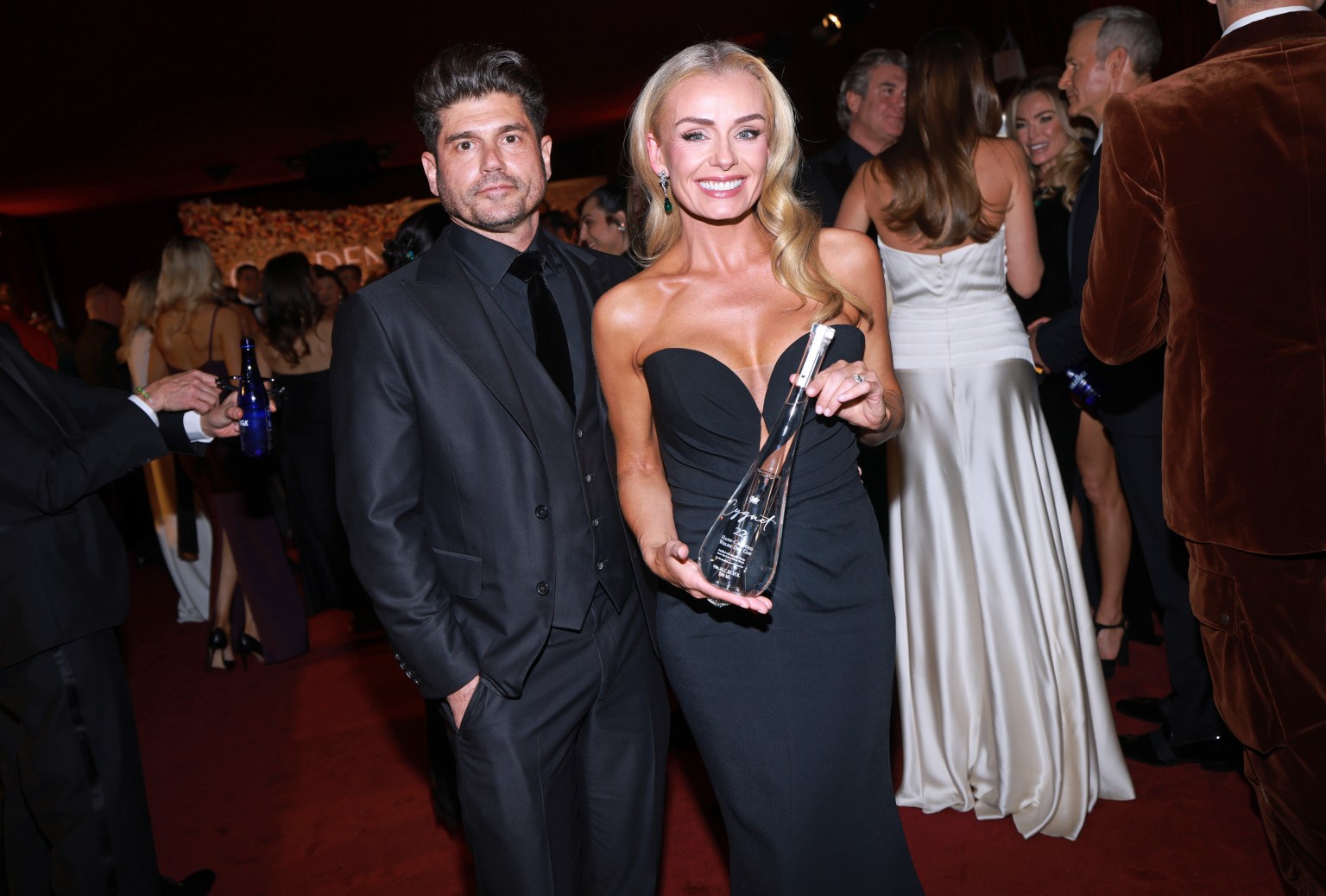 Katherine Jenkins and Andrew Levitas posing together on the Golden Globes red carpet, with Katherine holding a distinctive hand‑blown Cygnet gin bottle.