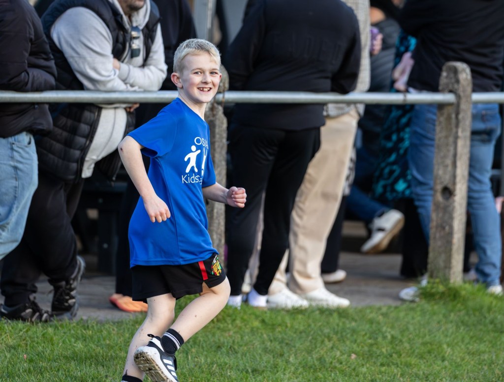 Osian running at Dunvant Rugby Club, looking back over his shoulder with crowds behind a metal barrier.