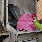Recycling worker tipping a pink recycling bag into the back of a kerbside recycling truck in Swansea.