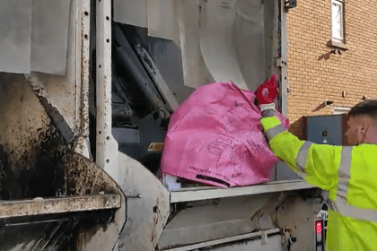 Recycling worker tipping a pink recycling bag into the back of a kerbside recycling truck in Swansea.
