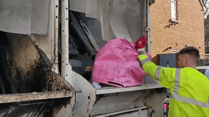 Recycling worker tipping a pink recycling bag into the back of a kerbside recycling truck in Swansea.