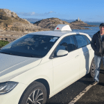 Driving instructor Mike Colwill standing beside his branded training car near Mumbles Lighthouse.