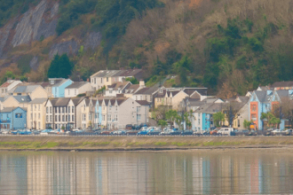 Scenic view of Mumbles from across the water, showing colourful buildings along the seafront.