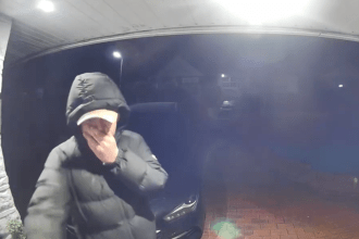 Man covering his face with his hand while trying to open a Baglan homeowner’s front door during a late‑night burglary attempt.