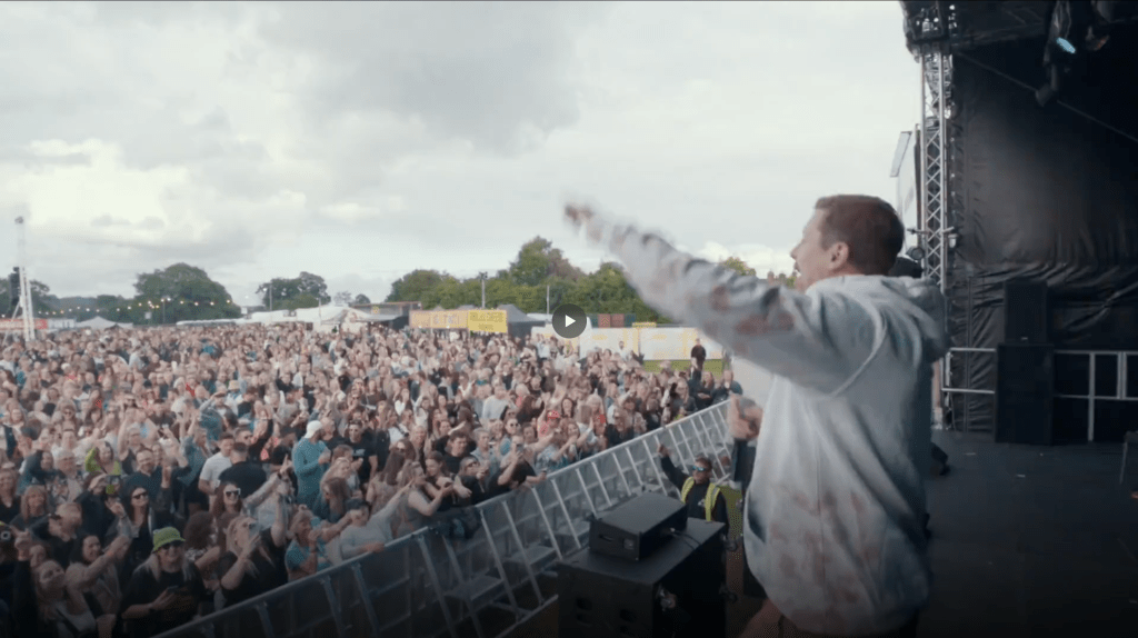 Dynamic image of a live music performance at an outdoor festival, showing a packed crowd and energetic stage presence.