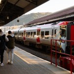 Modern Transport for Wales train stopped at Swansea Station platform with passengers walking nearby.