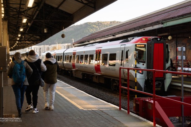 Modern Transport for Wales train stopped at Swansea Station platform with passengers walking nearby.