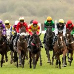 Horses racing at Ffos Las Racecourse on soft ground, with jockeys pushing for position near the home straight.
