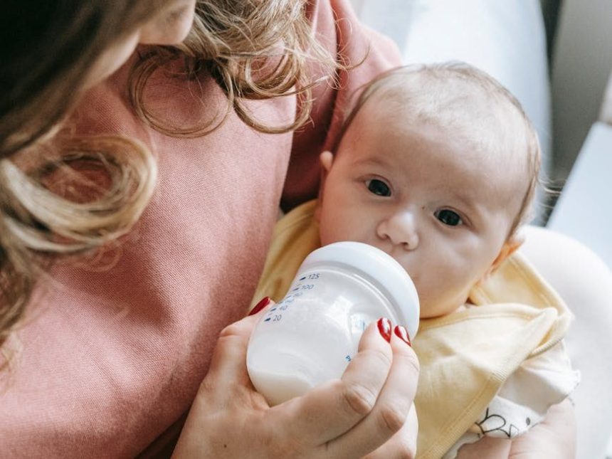 cute newborn drinking milk from bottle in hands of crop mom