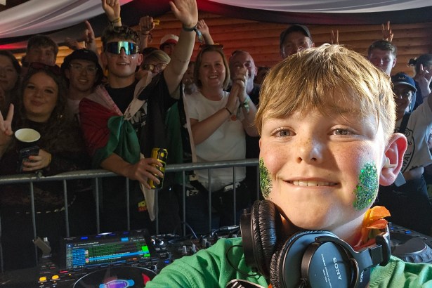 Efan Electro taking a selfie at the DJ desk with glitter on his cheeks, headphones around his neck and a crowd behind him.