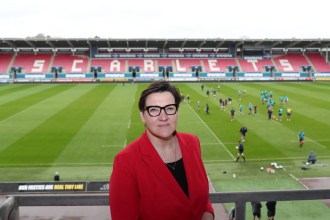 Tonia Antoniazzi standing pitchside at Parc y Scarlets with players training in the background.