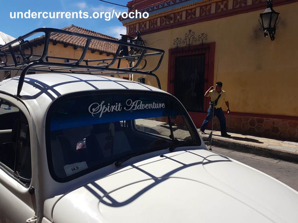 White VW Beetle with roof rack parked outside a colourful building in Mexico.